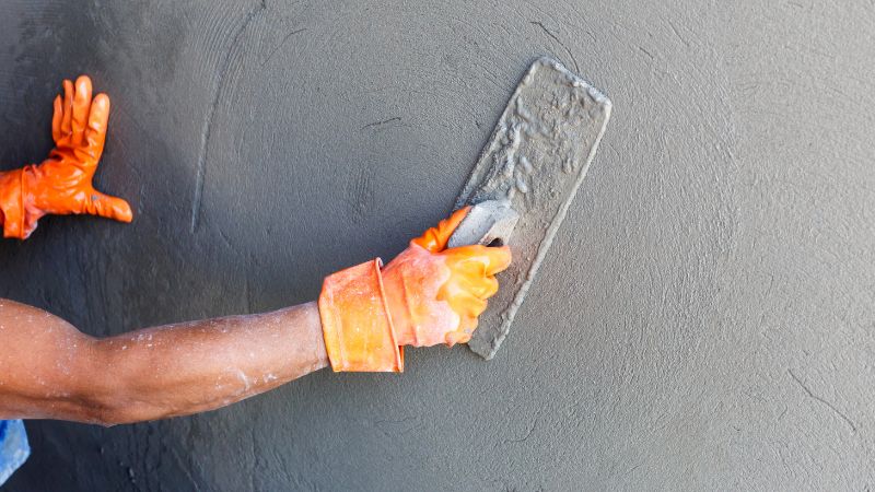 A man in an orange glove applies cement to a wall using a trowel.